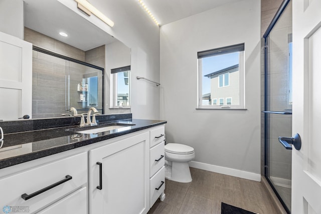 full bath featuring a healthy amount of sunlight, a shower stall, baseboards, and vanity