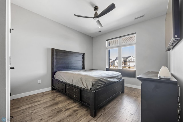 bedroom with a ceiling fan, visible vents, baseboards, and wood finished floors