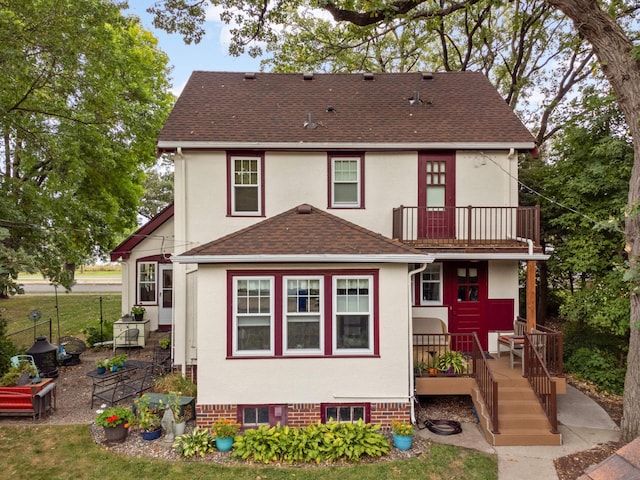 back of house featuring a balcony, a shingled roof, fence, and stucco siding