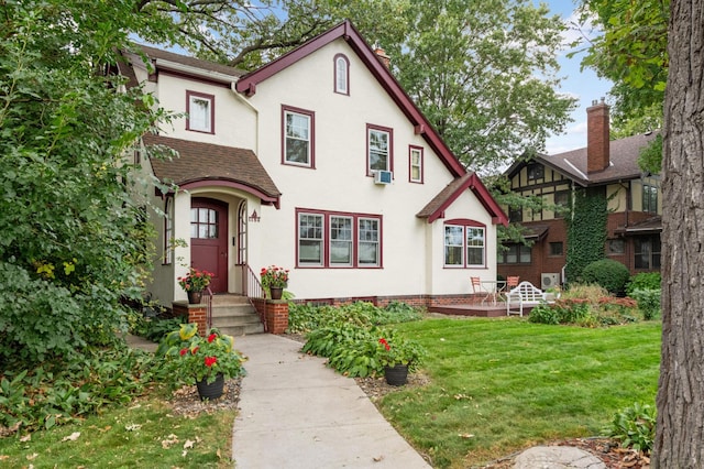 tudor-style house with roof with shingles, a front yard, and stucco siding