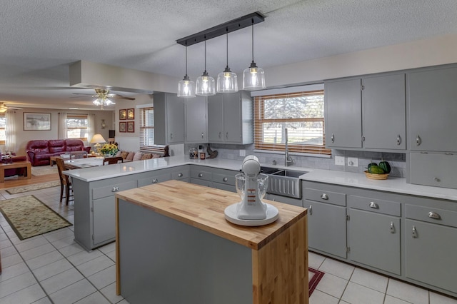 kitchen featuring light tile patterned floors, a ceiling fan, a peninsula, gray cabinetry, and wooden counters