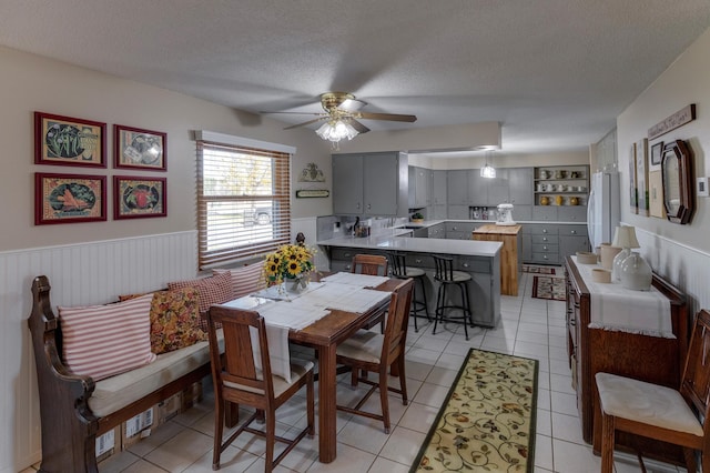 dining area featuring light tile patterned floors, a ceiling fan, a textured ceiling, and wainscoting