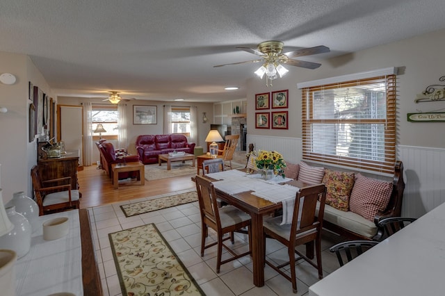 dining room with a wainscoted wall, ceiling fan, light tile patterned floors, and a textured ceiling