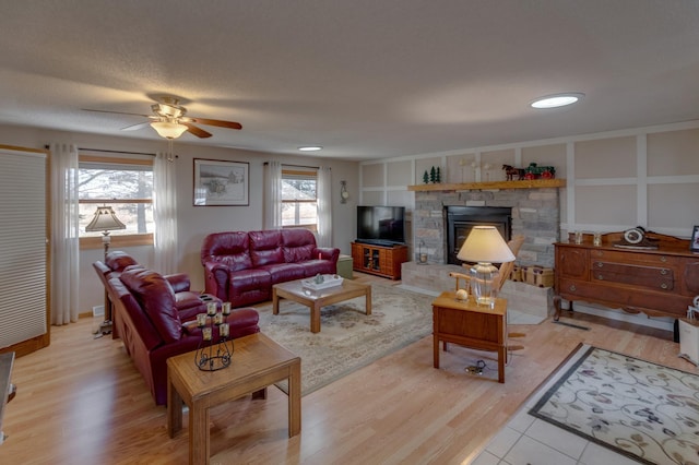 living room featuring a textured ceiling, light wood finished floors, a fireplace, and a ceiling fan