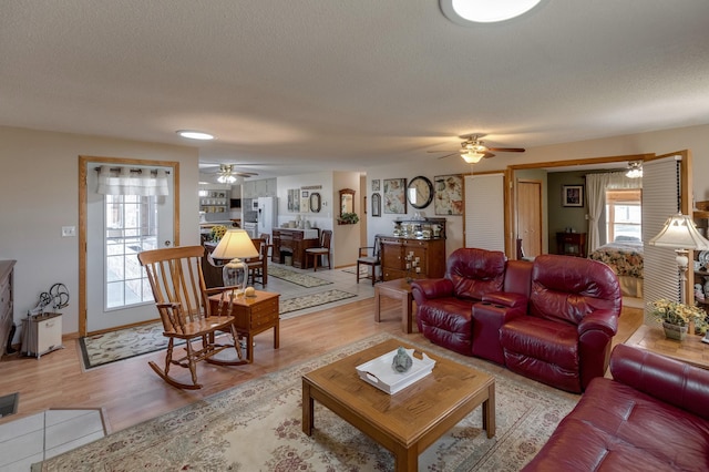 living room featuring light wood-style floors, ceiling fan, a textured ceiling, and baseboards