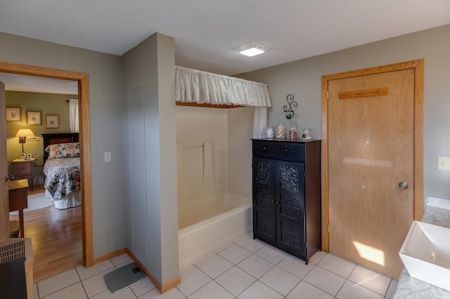 bathroom featuring a sink, ensuite bath,  shower combination, tile patterned flooring, and baseboards