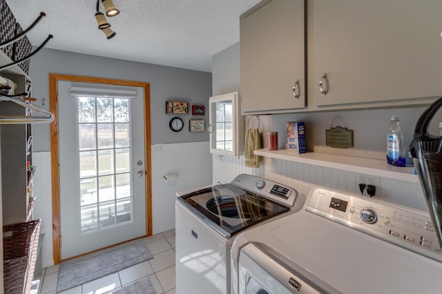 clothes washing area with cabinet space, a wainscoted wall, a textured ceiling, a healthy amount of sunlight, and washing machine and dryer