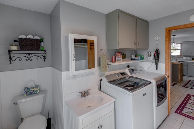 laundry area featuring laundry area, light tile patterned floors, a wainscoted wall, washing machine and dryer, and a sink