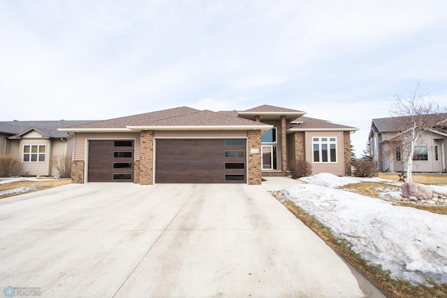 prairie-style home with a garage, concrete driveway, and brick siding