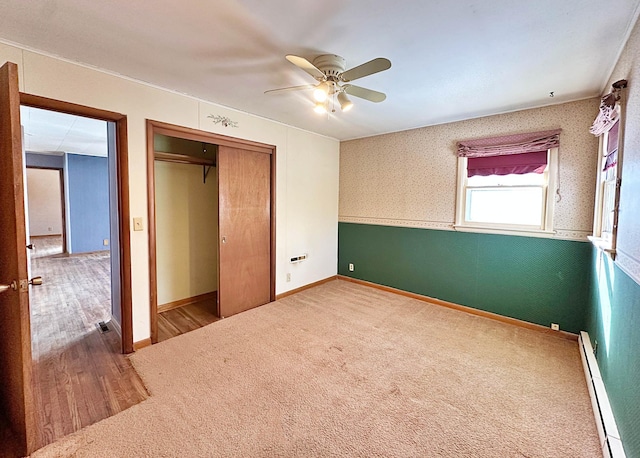 unfurnished bedroom with a closet, baseboard heating, carpet flooring, baseboards, and wallpapered walls