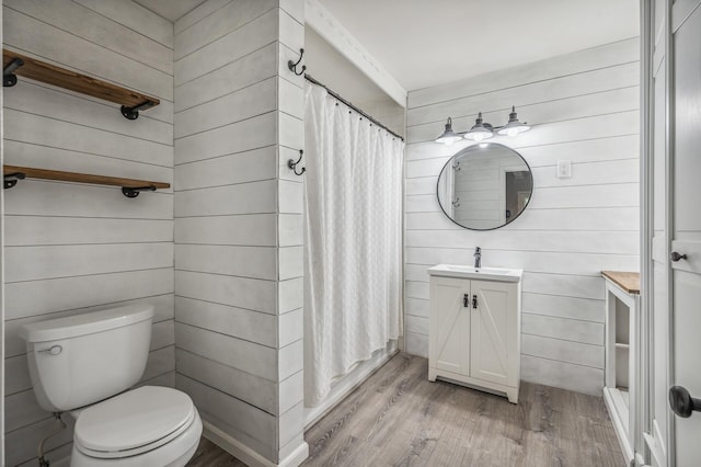 bathroom with wooden walls, toilet, a shower with curtain, wood finished floors, and vanity