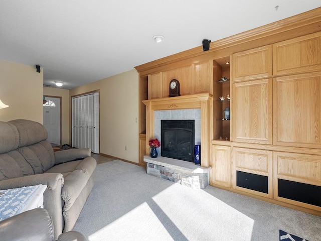 living area with built in shelves, a glass covered fireplace, light colored carpet, and baseboards