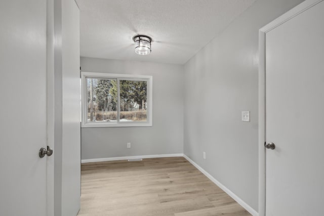 spare room featuring a textured ceiling, baseboards, and light wood-style floors