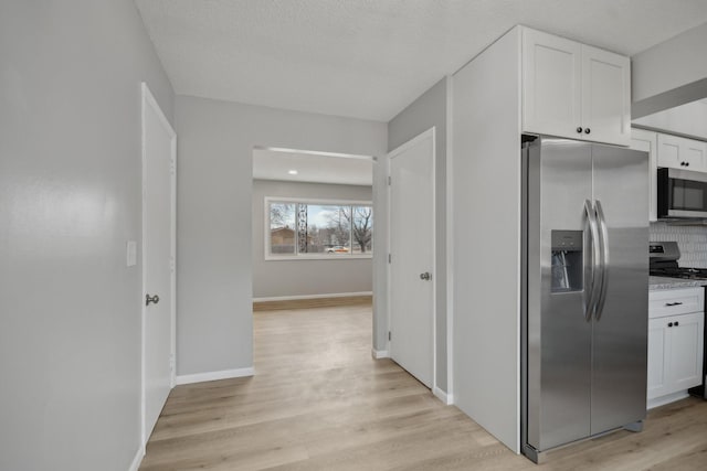 kitchen with baseboards, white cabinets, light wood-style flooring, appliances with stainless steel finishes, and a textured ceiling