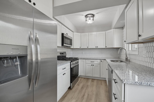 kitchen with appliances with stainless steel finishes, a sink, white cabinets, and tasteful backsplash