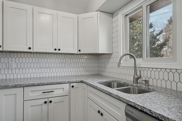 kitchen with light stone counters, tasteful backsplash, stainless steel dishwasher, white cabinets, and a sink