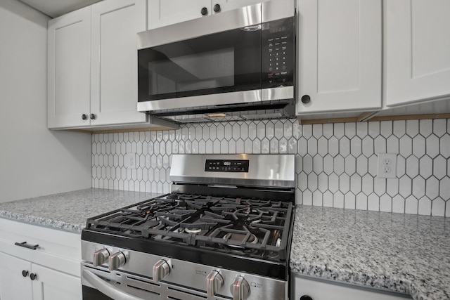 kitchen featuring stainless steel appliances, light stone countertops, white cabinetry, and decorative backsplash