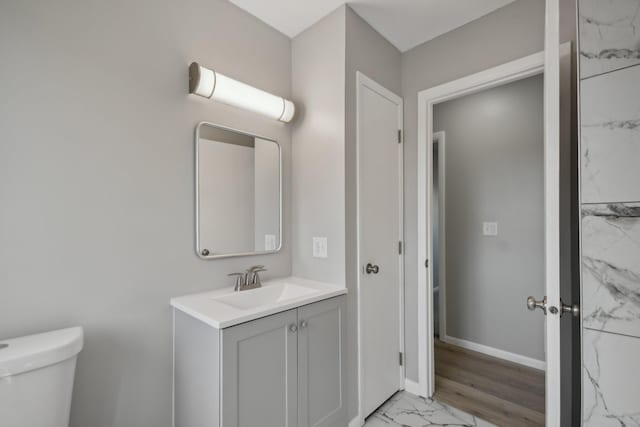 half bathroom featuring toilet, marble finish floor, baseboards, and vanity