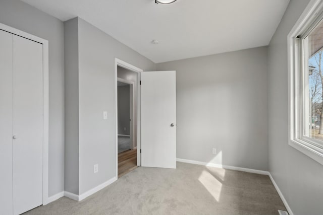 unfurnished bedroom featuring multiple windows, carpet, a closet, and baseboards