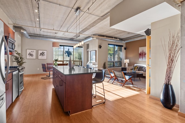 kitchen with a kitchen island, a kitchen breakfast bar, appliances with stainless steel finishes, light wood finished floors, and dark countertops