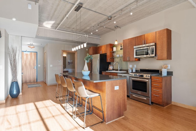 kitchen with dark countertops, a kitchen breakfast bar, a center island, stainless steel appliances, and a sink