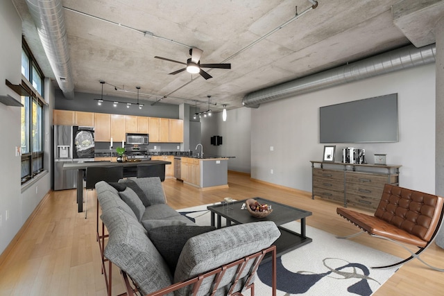 living area with ceiling fan, baseboards, rail lighting, and light wood-style floors