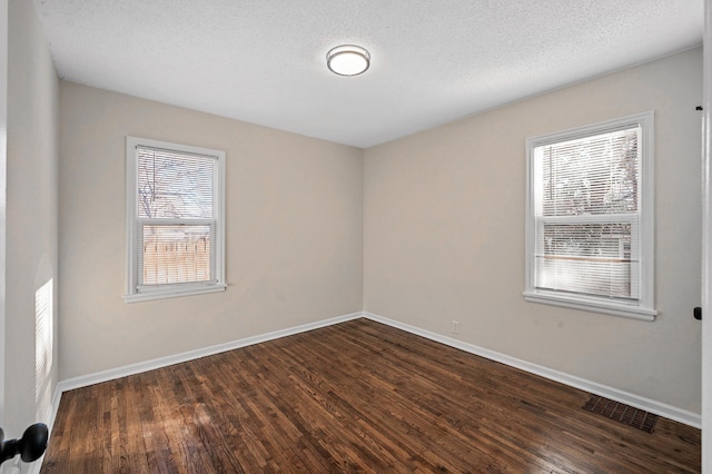 unfurnished room featuring dark wood-type flooring, visible vents, a textured ceiling, and baseboards