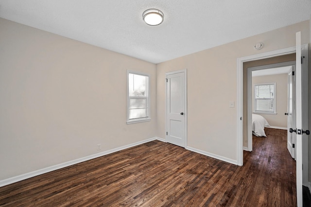 unfurnished bedroom featuring multiple windows, baseboards, dark wood finished floors, and a textured ceiling