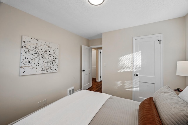 bedroom featuring visible vents, dark wood finished floors, a textured ceiling, and baseboards