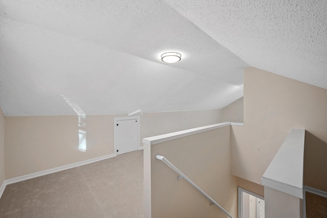 additional living space featuring a textured ceiling, vaulted ceiling, carpet flooring, and baseboards