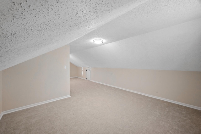 additional living space featuring carpet floors, baseboards, vaulted ceiling, and a textured ceiling