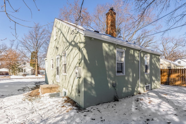 view of snow covered exterior featuring a chimney and fence