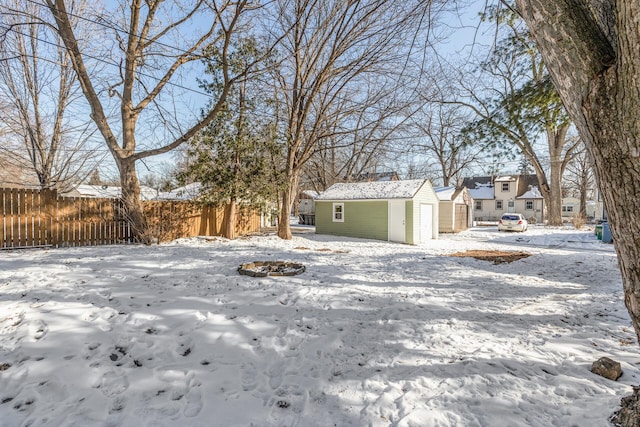 yard layered in snow featuring an outbuilding, a shed, a detached garage, and fence