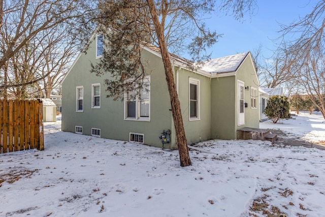 snow covered rear of property with fence and stucco siding