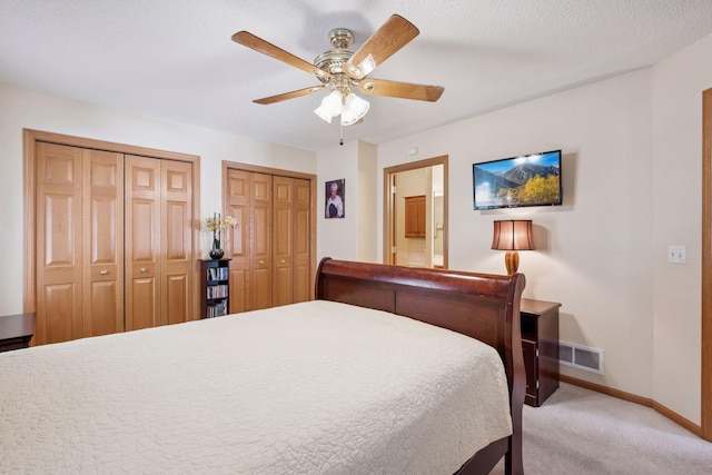 bedroom featuring light carpet, visible vents, baseboards, ceiling fan, and two closets