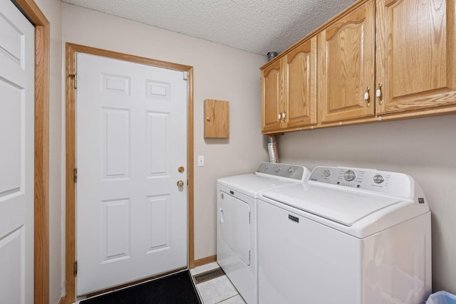 laundry room with cabinet space, washing machine and dryer, light tile patterned floors, and a textured ceiling