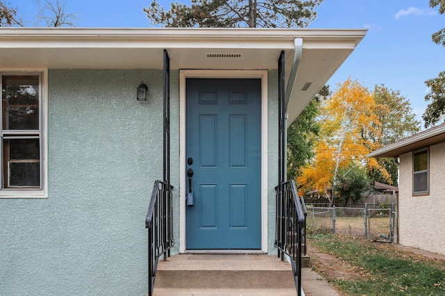 entrance to property with fence and stucco siding