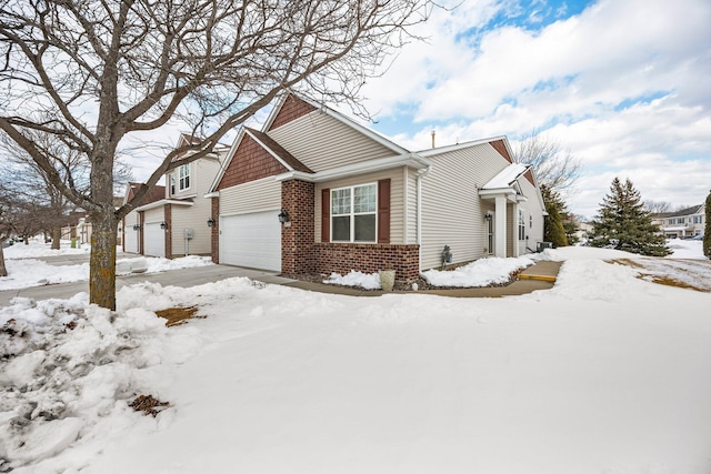 snow covered property with a garage and brick siding