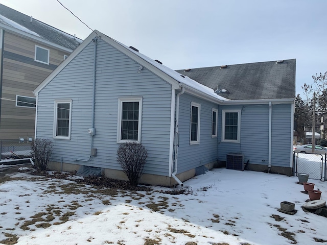 snow covered property with a shingled roof and fence