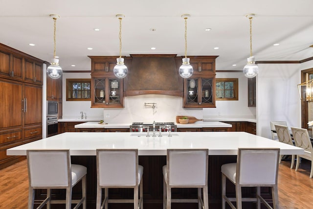 kitchen featuring oven, a spacious island, a sink, built in microwave, and custom range hood