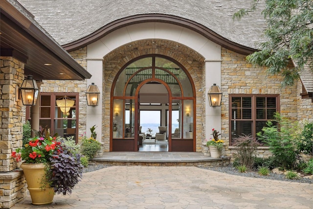 doorway to property with stone siding and a shingled roof