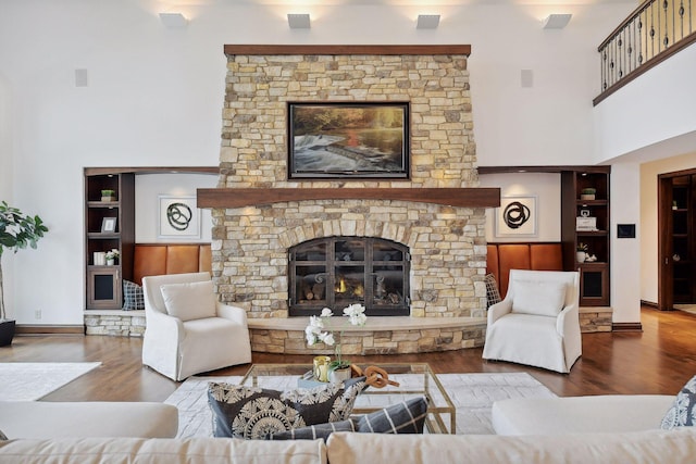 living area featuring baseboards, a stone fireplace, a towering ceiling, and wood finished floors