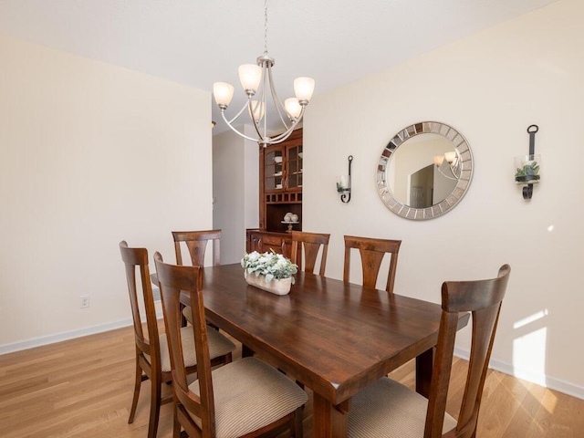 dining room with a chandelier, light wood-style flooring, and baseboards