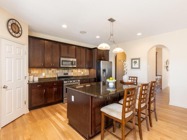 kitchen featuring arched walkways, a center island, light wood finished floors, tasteful backsplash, and appliances with stainless steel finishes