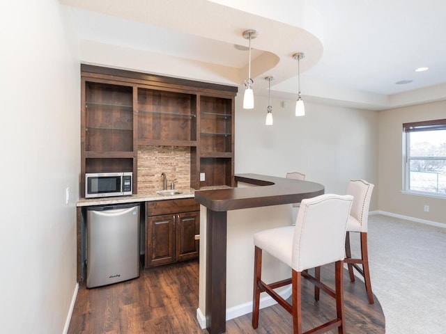 bar with dark wood-style flooring, stainless steel appliances, tasteful backsplash, a sink, and baseboards