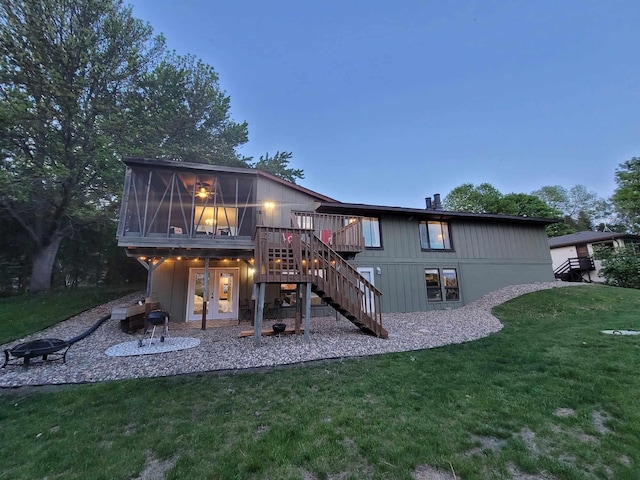 back of house featuring a lawn, a sunroom, a fire pit, a wooden deck, and stairs