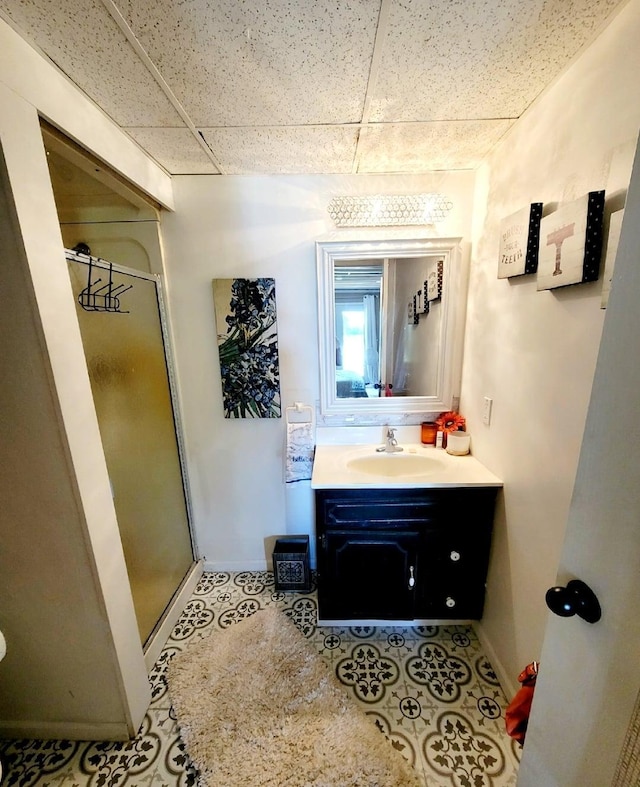 bathroom with a paneled ceiling, baseboards, a shower stall, and vanity