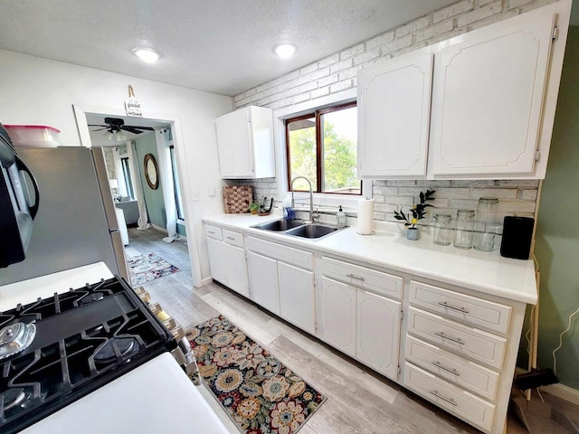 kitchen with range with gas cooktop, light countertops, light wood-style floors, white cabinetry, and a sink