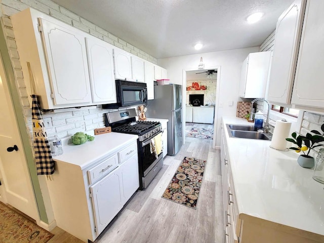 kitchen with stainless steel appliances, light countertops, light wood-type flooring, white cabinetry, and a sink