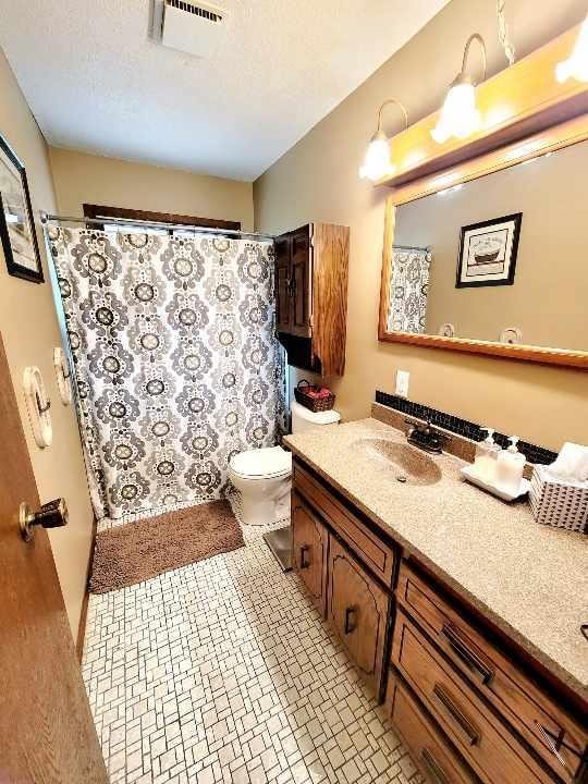 full bathroom with visible vents, toilet, tile patterned floors, a textured ceiling, and vanity